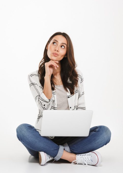 pensive-brunette-woman-shirt-sitting-floor-with-laptop-computer-looking-up-gray